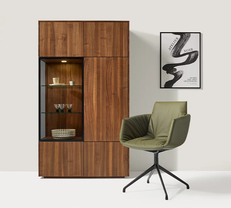 Elegant lui casual dining chair in olive leather on a swivel base in matt black in front of a filigno display cabinet in solid walnut and smoked glass
