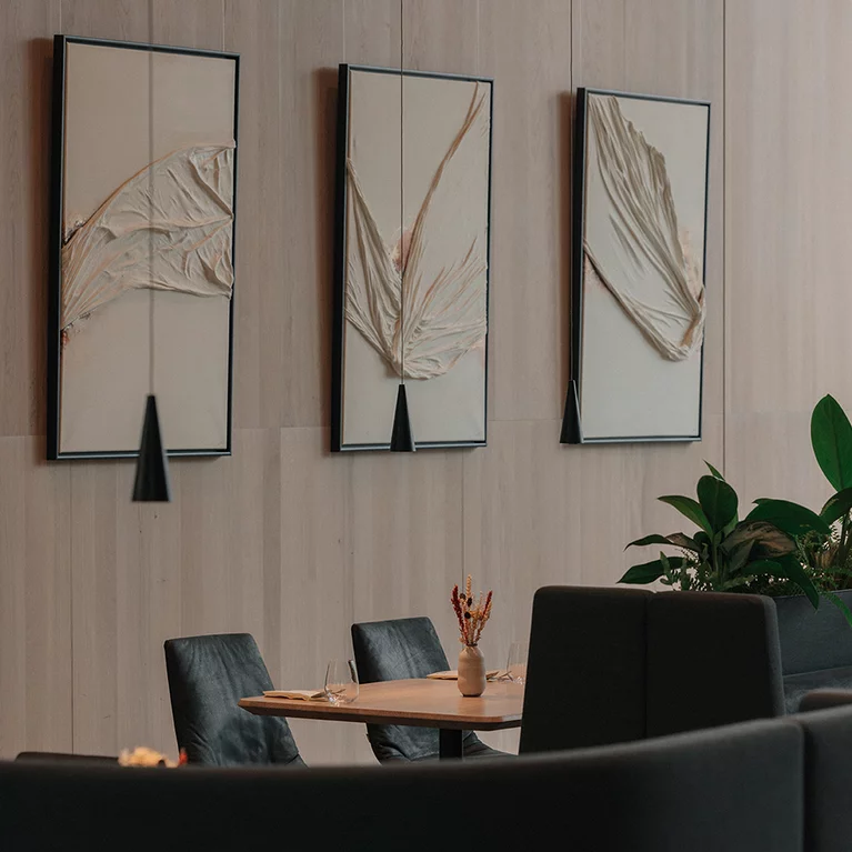 lui chairs with natural leather upholstery at restaurant tables with oak top in front of solid wood wall