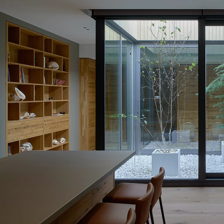 Atrium with trees stylishly surrounded by customised TEAM 7 furniture in Venetian oak and a cubus shelving unit with Venetian oak drawers