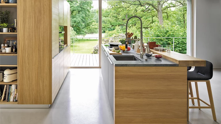 wooden kitchen linee in oak with worktop in natural stone and fronts with handle strip in stainless steel finish and bar top with ark bar stools