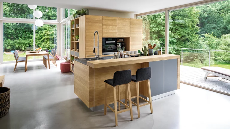 Massivholzküche mit Farbglas Fronten, Arbeitsplatte aus Naturstein und Barelement mit Barhockern linee Massivholzküche in Eiche mit Farbglas Fronten mittelgrau matt, Arbeitsplatte aus Naturstein und Barelement mit ark Barhockern