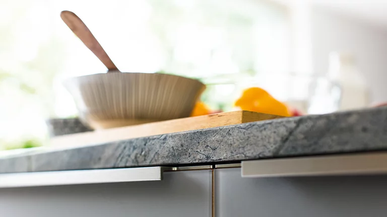 kitchen linee in oak with coloured glass fronts medium grey matt with handle profile in stainless steel finish and worktop natural stone