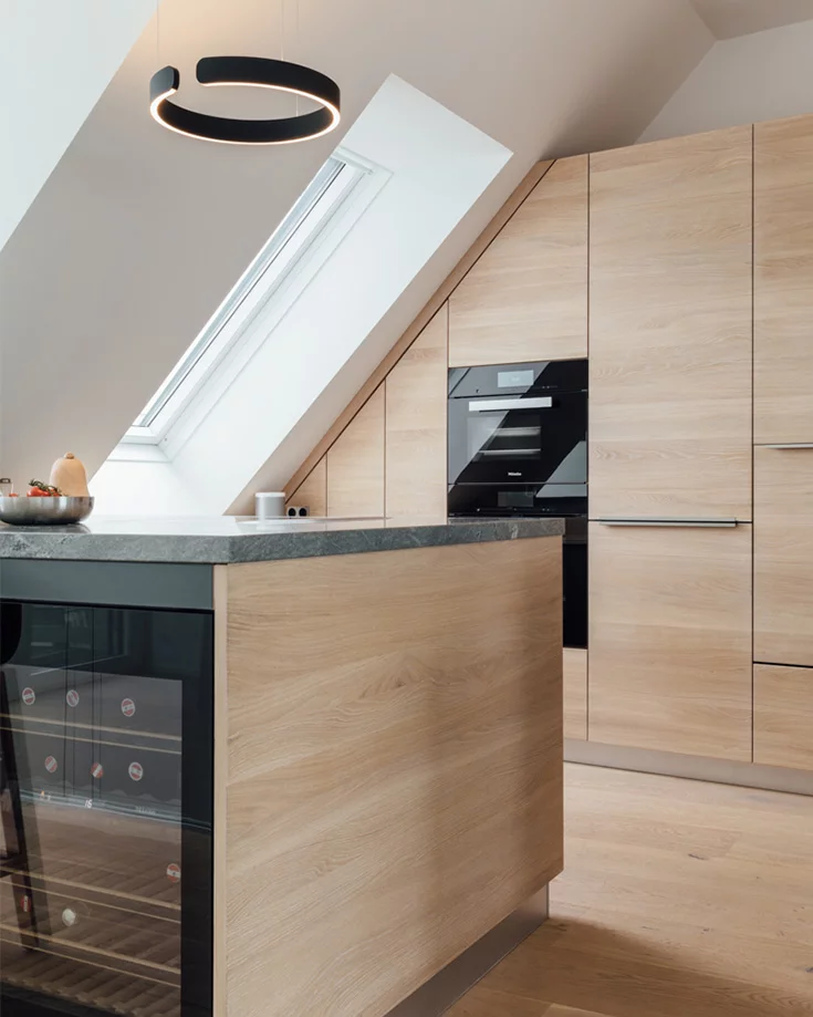 Customised kitchen unit fitted into the sloping ceiling and cooking island with wine fridge in white oak oil