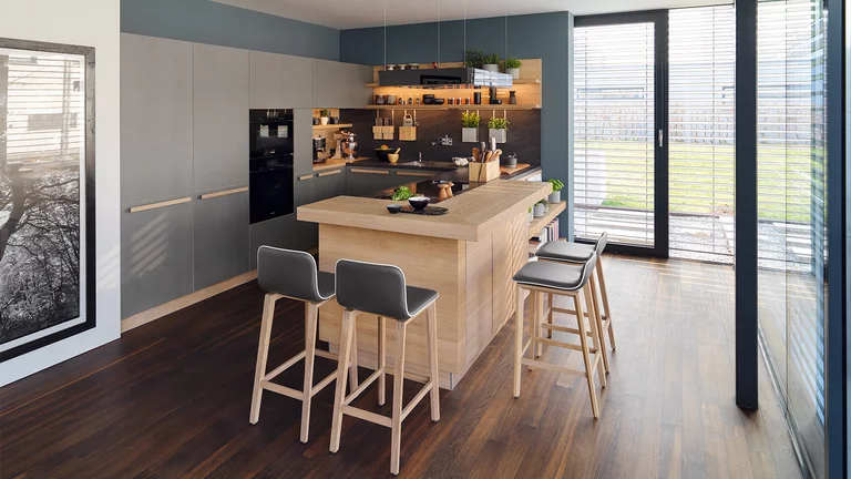 Naturholzküche cera line beleuchtet in Eiche Weißöl mit Fronten und Arbeitsplatte in Keramik und Barplatte mit ark Barhockern in Leder