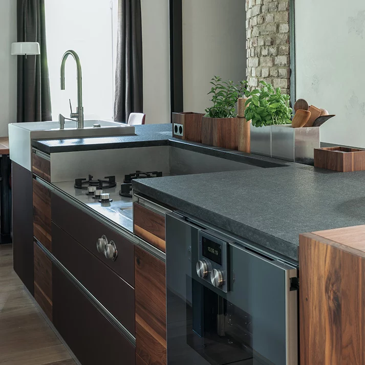 Massivholzküche in Nussbaum mit Arbeitsplatte aus Stein und Farbglasfronten anthrazit matt