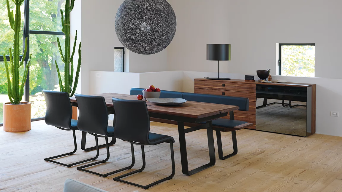 modern dining table nox made of natural wood extendable in walnut with the magnum cantilever chairs upholstered and the nox bench