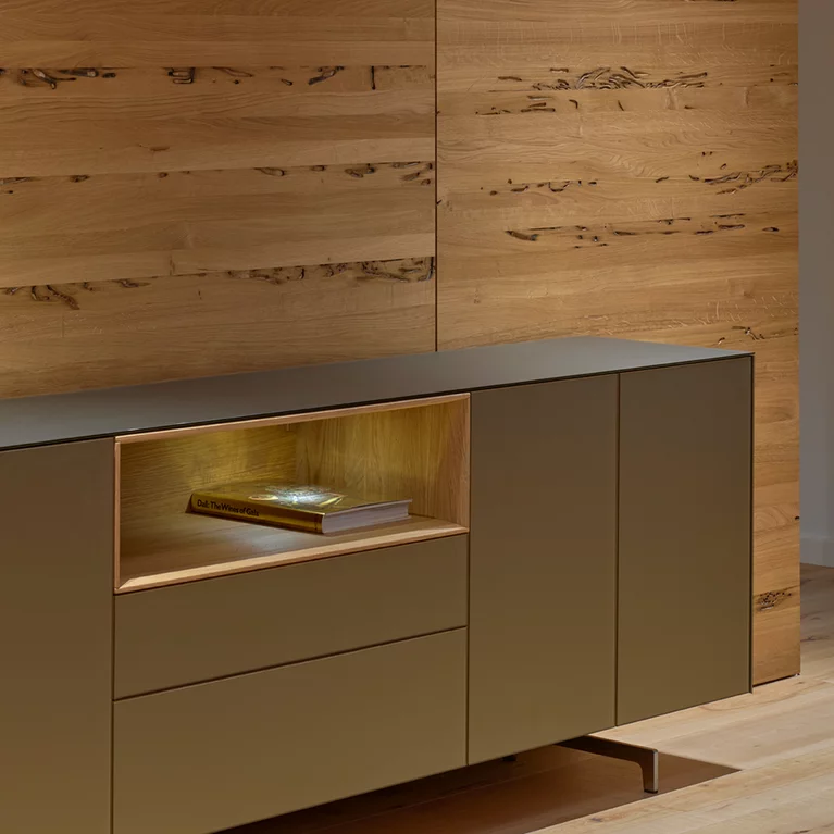 cubus pure sideboard with coloured glass casing on metal runners and illuminated oak niche in front of wooden wall in venetian oak