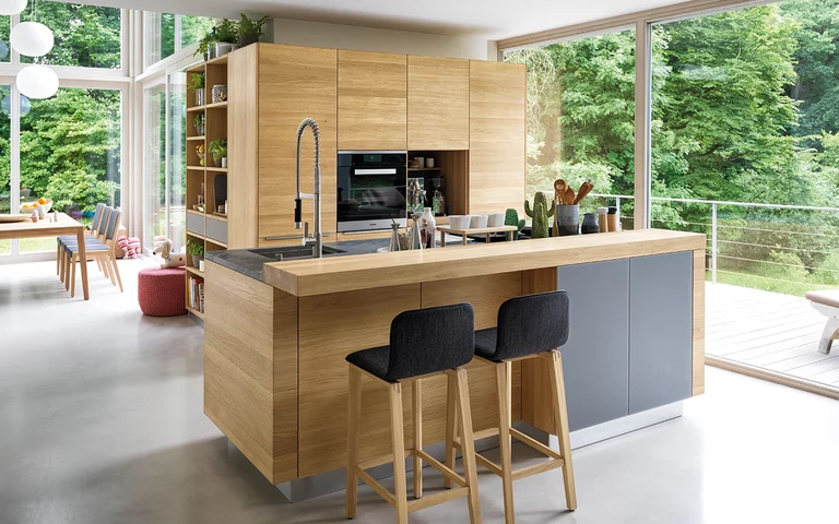 linee solid wood kitchen in oak with coloured glass fronts medium grey matt, worktop in natural stone and bar element with ark bar stools