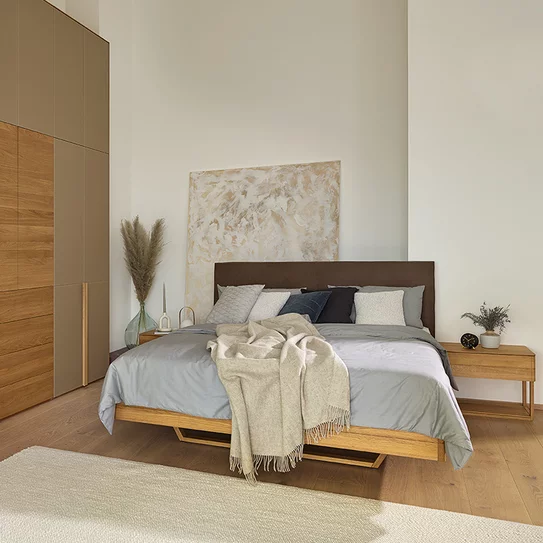 Float solid wood bed with leather headboard and float bedside cabinet next to soft hinged door wardrobe with top unit and coloured glass fronts in natural oak oil