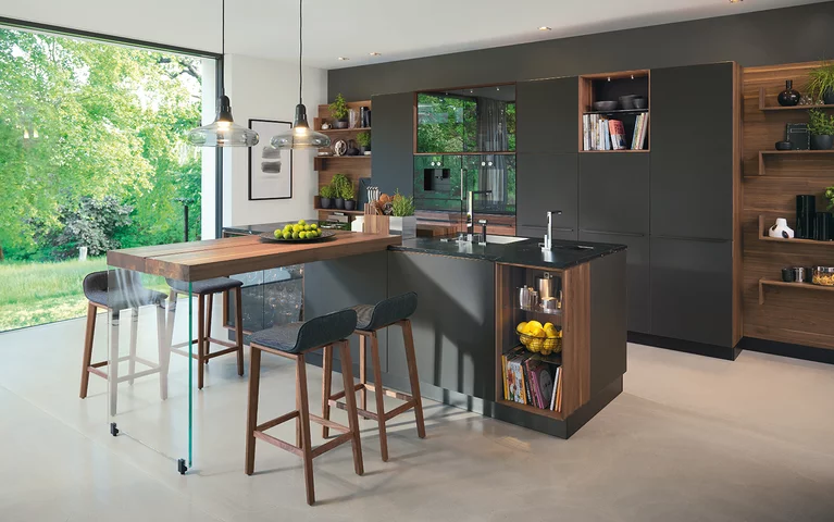 black line Naturholzküche in Nussbaum mit Farbglas Fronten, Kücheninsel mit Arbeitsplatte aus Naturstein und Anbautisch mit ark Barhockern
