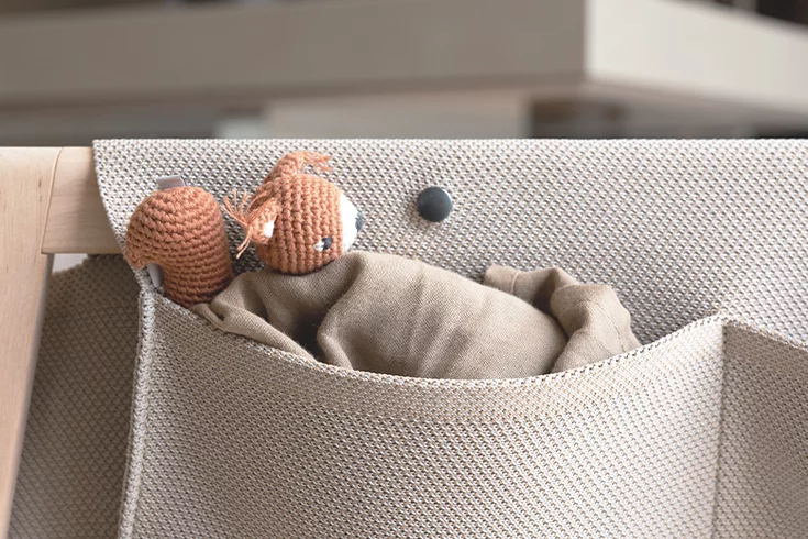 wooden baby cot with soft knitted fabric and fabric bags, detailed view baby cot in alder white oil with soft knitted fabric and practical fabric pockets, detailed view