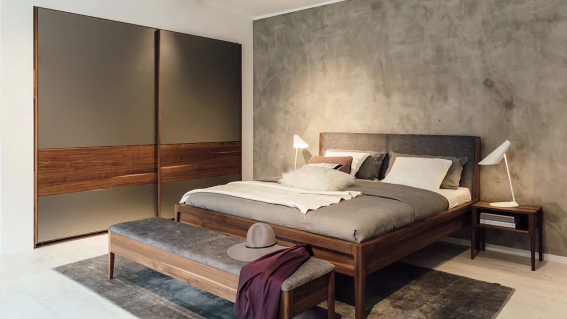 valore Schwebetürenschrank mit Farbglasfronten zusammen mit dem mylon Bett, mylon Bank und mylon Nachtkästchen in der Holzart Nussbaum