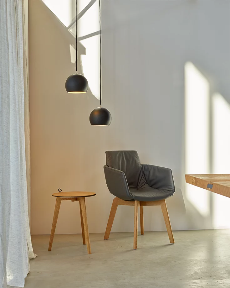 hi! round side table in oak next to the grand lui upholstered chair in leather with wooden frame