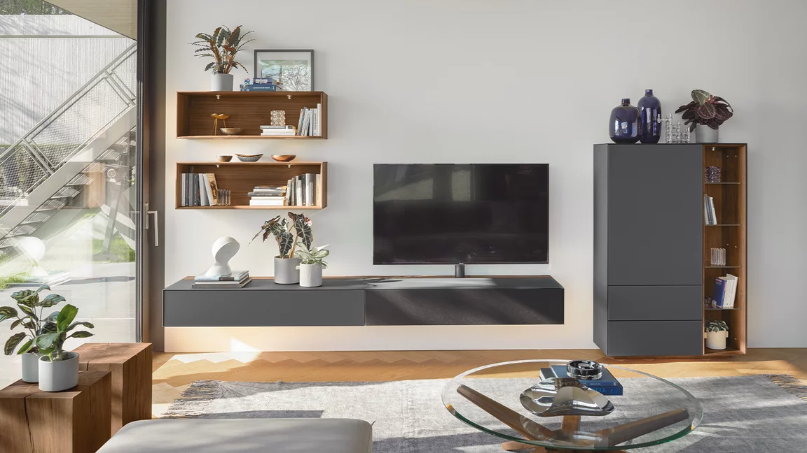 dunkle Wohnwand cubus pure aus Glas kombiniert mit beleuchtete Regale und dem stern Couchtisch aus Nussbaum massiv in modernem Wohnwand