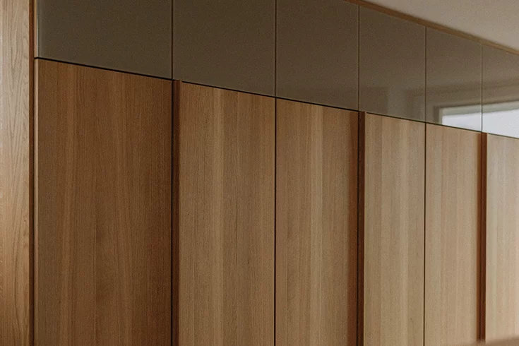 Floor-to-ceiling solid wood hinged door wardrobe soft in natural oak oil with handle strips and some doors in coloured glass