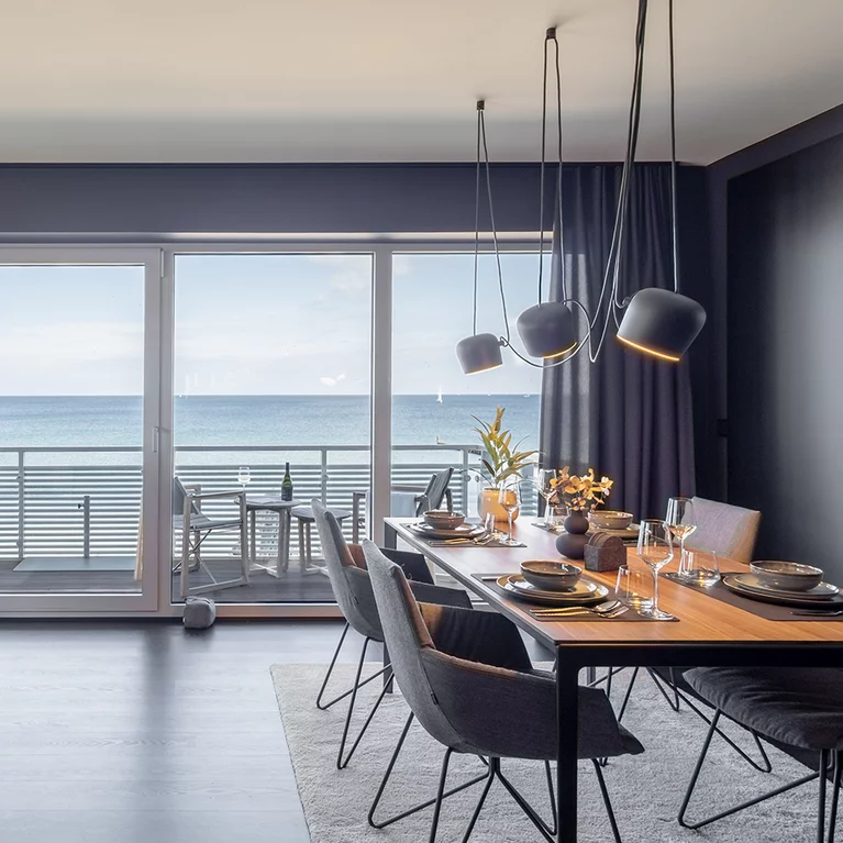 Elegante lui legér Stühle mit Stoffbezug und Drahtgestell an tak Tisch in Nussbaum massiv vor großer Fensterfront mit Meerblick