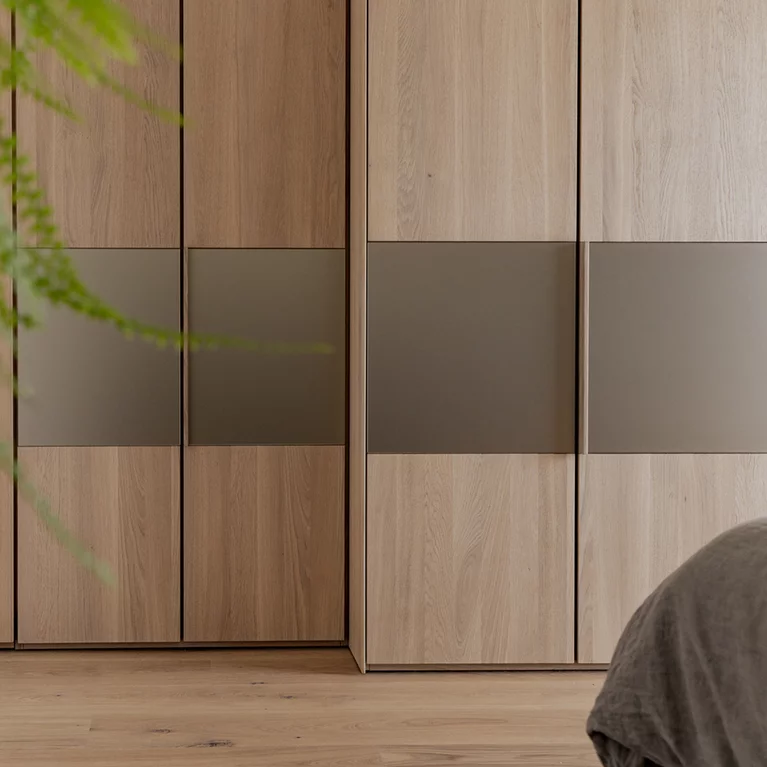 Massivholz Drehtuerenschrank in Eiche Weißöl mit integrierten Holzgriffleisten und Farbglaselementen in bronze Massivholz Drehtuerenschrank valore in Eiche Weißöl mit integrierten Holzgriffleisten und Farbglaselementen in bronze